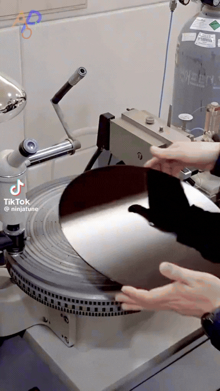 Hands lifting a freshly pressed vinyl record off a record press